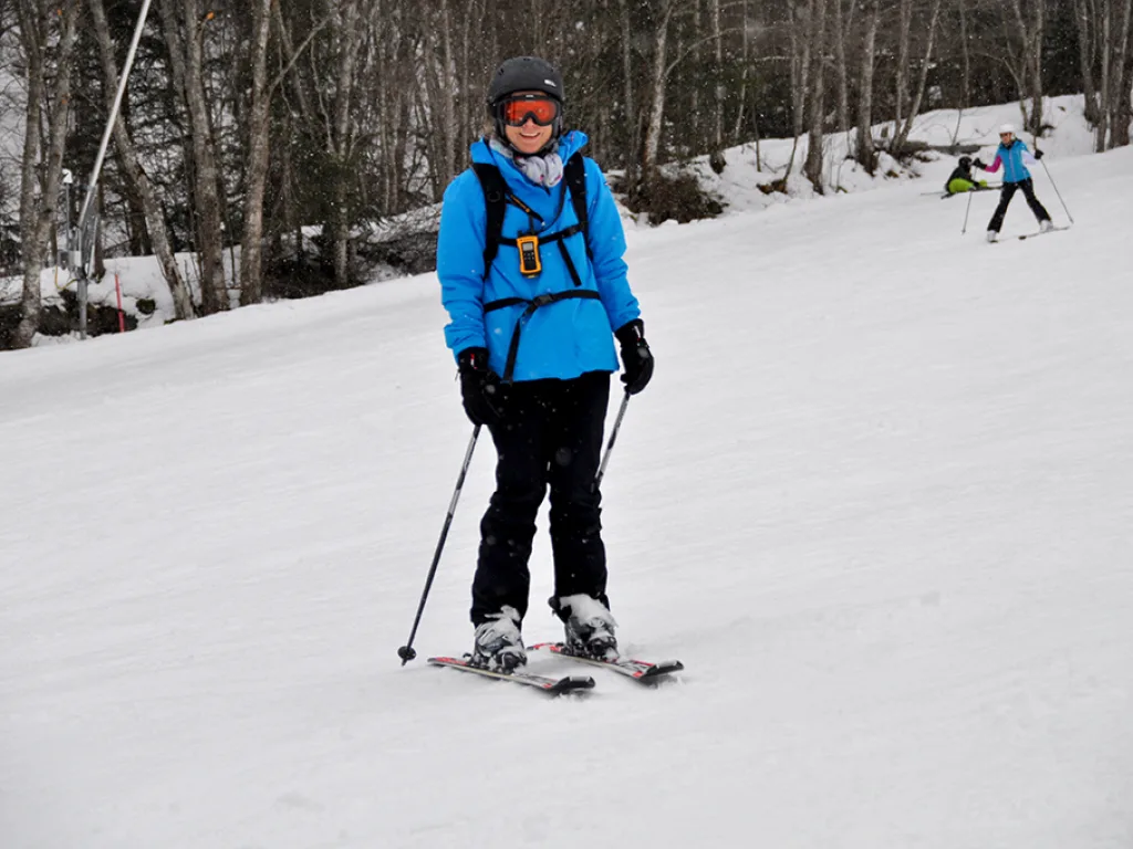 Skifahrerin in blauer Jacke am Waldrand.